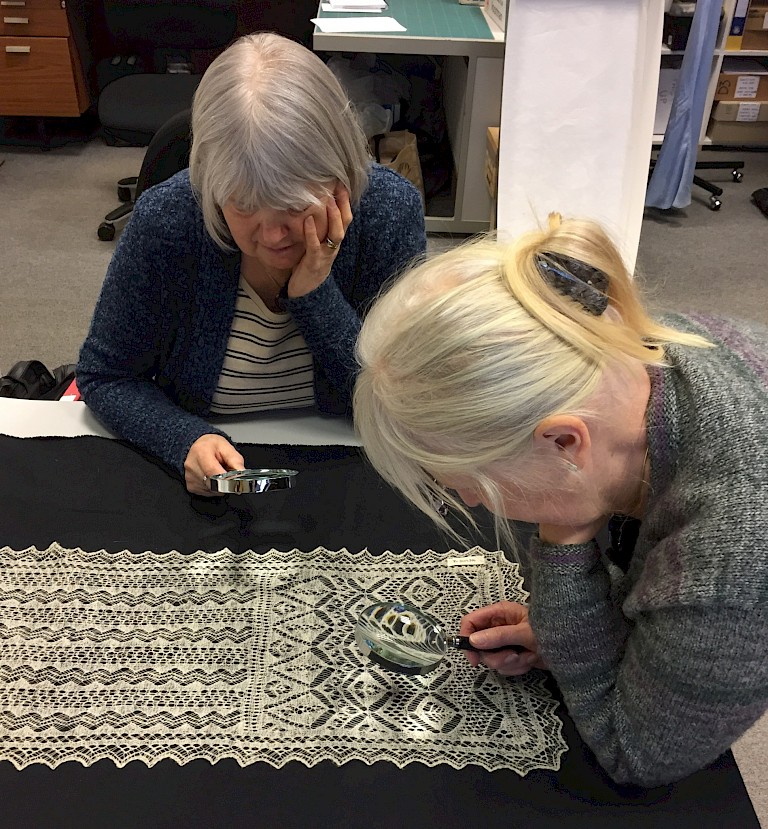Kathleen (left) and Anne (right) investigating the centre of a diamond motif on an early fine lace scarf.